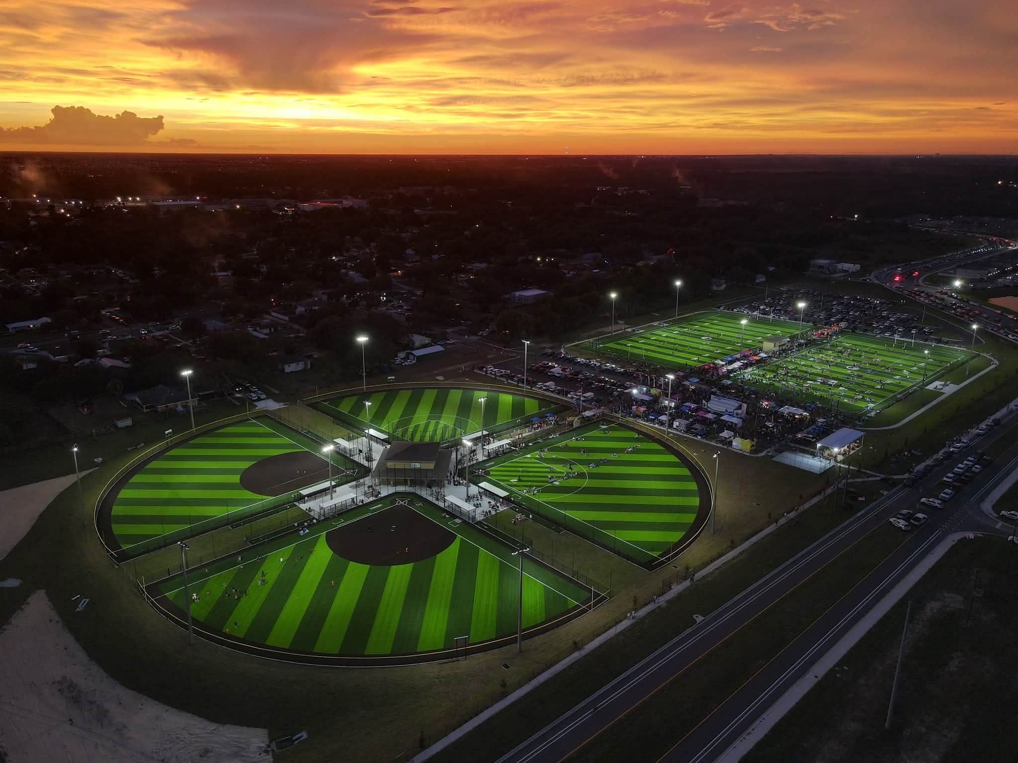 Aerial view at sunset of a lit four-field softball complex and football fields built by Legacy Sports Construction